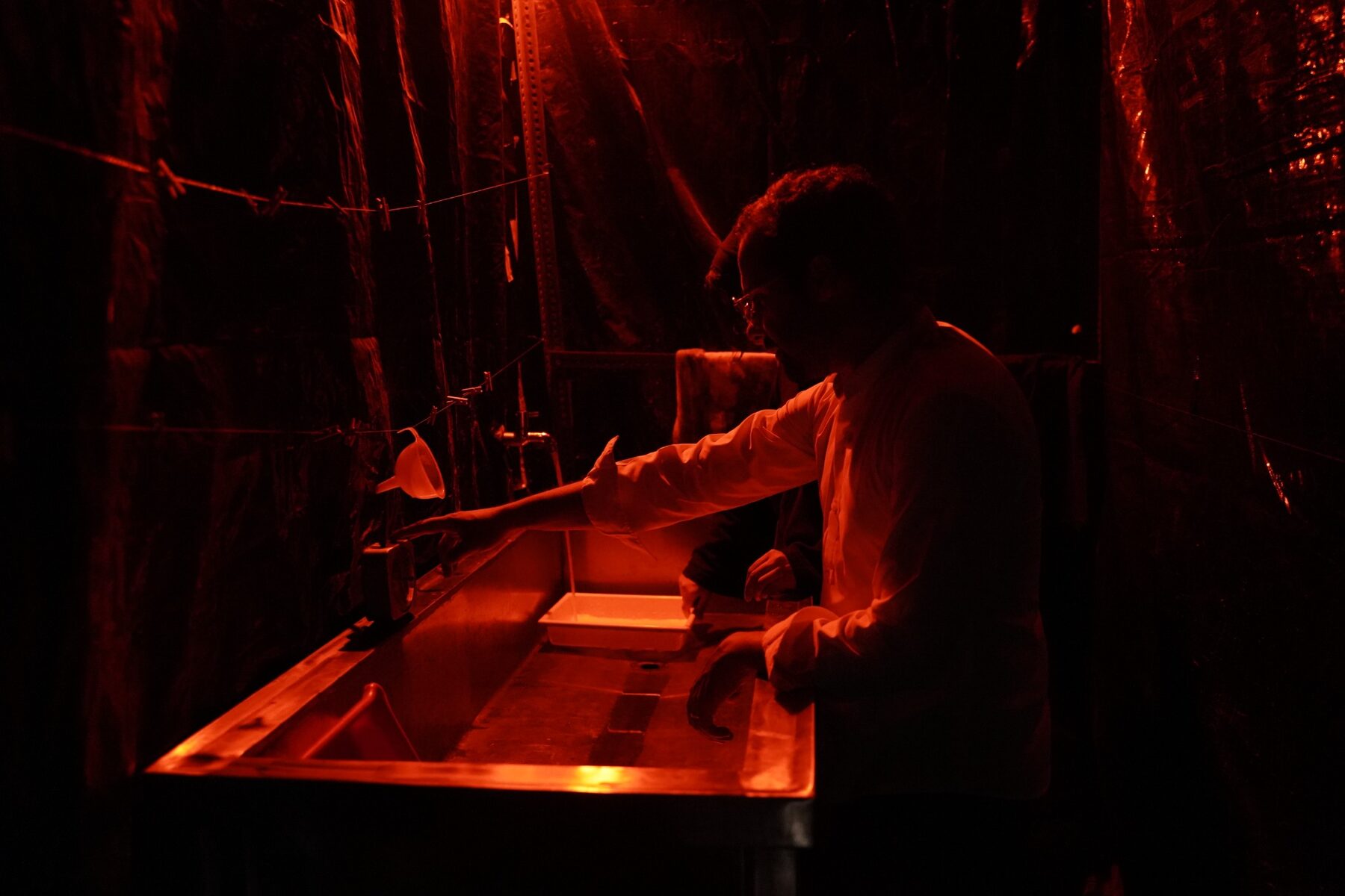 An artist hand-processing photographic material under red darkroom light